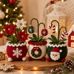 May include: Three crocheted potted plants featuring festive holiday themes. The first pot is red with a white snowflake and poinsettia flowers. The second is white with a wreath and hanging ornaments. The third is green with a Santa Claus face.