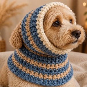 May include: A light brown dog wearing a crocheted snood hood featuring horizontal stripes in alternating shades of blue and beige, finished with a textured cream-colored border around the face opening that frames the dog's head and neck.