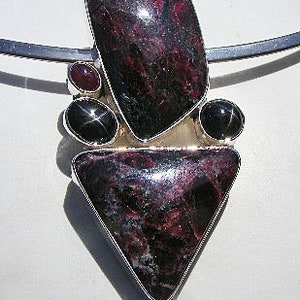 May include: A silver pendant with a triangular shaped black and red gemstone, surrounded by three smaller black gemstones.
