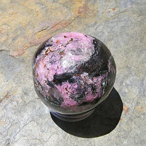 May include: A polished sphere of black and pink gemstone with a smooth, shiny surface.