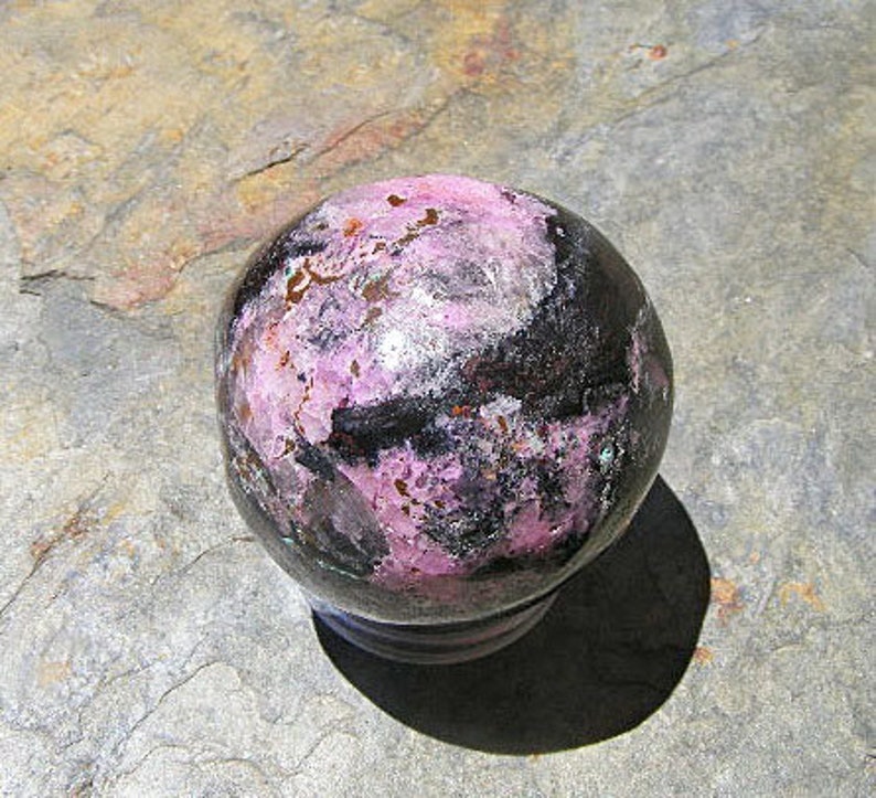 May include: A polished sphere of black and pink gemstone with a smooth, shiny surface.