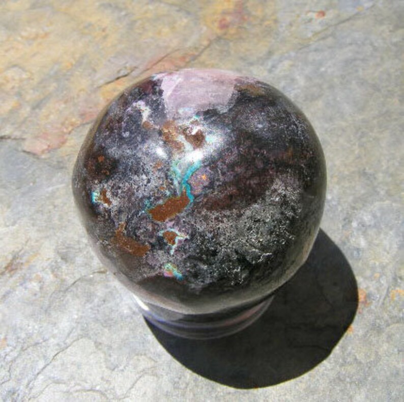 May include: A dark gray, black, and copper sphere with a smooth, polished surface. The sphere has a variety of colors and patterns, including pink, blue, and white.