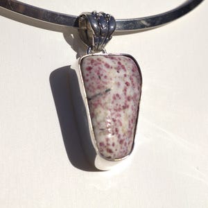 Puede incluir: Un colgante de plata con una piedra rosa y blanca. La piedra está engastada en un bisel de plata y tiene una forma rugosa y natural.