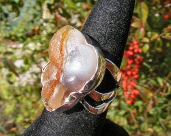 May include: A silver ring with a large, white and orange agate stone. The stone is shaped like a flower and has a natural, organic look.