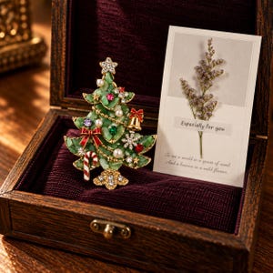 May include: A gold-toned Christmas tree brooch featuring green stone fragments, white pearls, red and gold bows, a candy cane, a star, and clear crystals. Beside it is a white card with a dried flower and the text Especially for you.