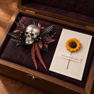 May include: A wooden box with a purple velvet lining containing a silver skull ornament surrounded by black and red foliage, alongside a white card featuring a yellow sunflower and the printed text Especially for you on a small paper strip.