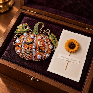 May include: An orange pumpkin brooch featuring iridescent crystals, black bat and spiderweb motifs, and a white crescent moon. Beside it, a small card displays a yellow sunflower pin with the printed text "Especially for you" in black ink.