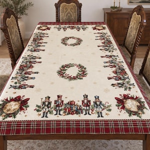 Könnte beinhalten: Eine rechteckige Tischdecke mit cremefarbener Mitte, die ein wiederkehrendes Muster aus Nussknackerfiguren, Stechpalmenkränzen und Geschenkhaufen zeigt. Der Rand besteht aus dunkelrotem Schottenkaro mit goldenen Ornamenten und roten Schleifen.