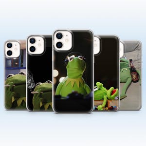 May include: A collection of five clear smartphone cases, each featuring a different graphic of a green frog puppet. The designs show the frog in various poses, including wearing headphones, holding a cigarette with smoke, and reclining with bottles.