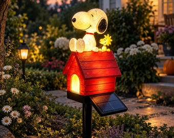 May include: A solar-powered garden light featuring a white Snoopy figure with a red collar and a small yellow Woodstock figure sitting on top of a red doghouse. The doghouse has a glowing yellow interior and a black solar panel attached.