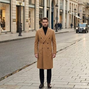 May include: A camel-colored double-breasted wool coat with wide lapels and dark buttons, worn over a black turtleneck sweater and dark trousers, paired with brown leather dress shoes on a city street.