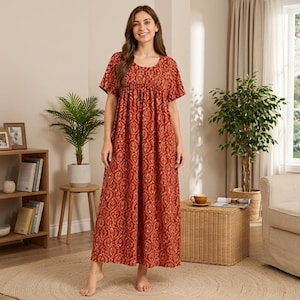May include: A floor-length, short-sleeved dress in a rust-orange hue featuring a repeating white and gold teardrop-shaped pattern. The garment has a round neckline and a gathered bodice that flows into a loose, relaxed skirt silhouette.