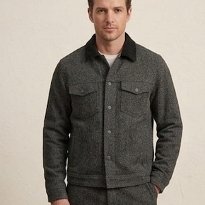 May include: A charcoal grey textured jacket featuring a solid black collar, a button-down front closure, and two chest pockets with buttoned flaps. The jacket is constructed from a heathered fabric and is paired with matching charcoal grey trousers.