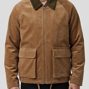 Könnte beinhalten: Eine hellbraune Wildlederjacke mit einem dunkel olivgrünen Cordkragen, einem durchgehenden Frontreißverschluss und zwei großen aufgesetzten Taschen mit Klappen auf der Vorderseite. Die Jacke hat einen Kordelzugsaum mit zwei herabhängenden Kordeln.