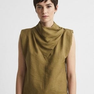 Peut inclure: Un haut sans manches vert olive doté d'un col bénitier drapé et montant avec deux petits boutons sur l'épaule gauche. Le vêtement présente des épaules structurées et un ourlet droit, confectionné dans un tissu uni à la texture visible.