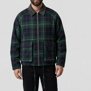 Puede incluir: Una chaqueta con cremallera que presenta un patrón de cuadros en verde, azul marino y rojo fino. La chaqueta incluye un cuello gris oscuro sólido, una cremallera frontal completa y dos grandes bolsillos cuadrados de parche. El dobladillo tiene dos cordones.