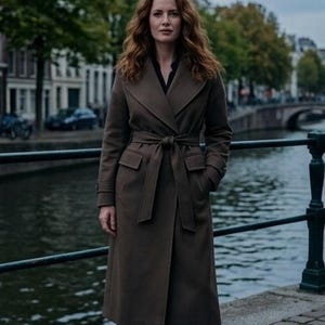 May include: A long, dark brown wool-blend coat featuring a wide lapel, long sleeves, and a matching fabric tie belt at the waist. The coat includes two front flap pockets and falls to a mid-calf length, worn over a black shirt.