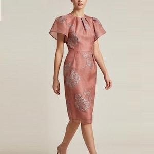 Peut inclure: Une robe mi-longue rose poudré dotée de manches courtes évasées, d'une encolure ronde avec des plis subtils et d'une silhouette structurée. Le tissu est orné d'un motif floral argenté métallique texturé sur tout le corsage et la jupe.