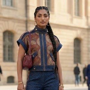 May include: A short-sleeved, high-neck jacket featuring a dark blue denim trim and a central panel with a brown and gold paisley pattern. The jacket has a front zipper, two front pockets, and is paired with matching dark blue patterned trousers.