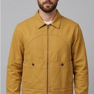 Puede incluir: Una chaqueta con cremallera de color amarillo mostaza que presenta un cuello en punta, mangas largas y dos bolsillos delanteros con cierre de botón. La chaqueta tiene una costura semicircular distintiva en el pecho y se usa sobre una camisa blanca y jeans azules.