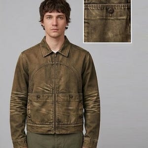 Pode incluir: Uma jaqueta castanho-oliva de manga comprida com fecho frontal, gola pontiaguda e dois bolsos frontais com fecho de botão. O tecido apresenta um acabamento desgastado com desbotamento visível nos cotovelos e nas costuras do peito.