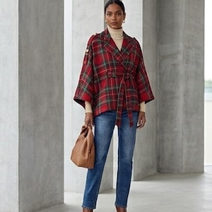May include: A red and green plaid wrap jacket with a tie waist, worn over a beige turtleneck sweater and blue denim jeans. The outfit includes a tan leather handbag and brown leather boots, creating a coordinated ensemble.