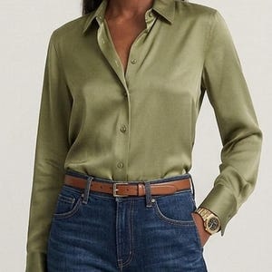 May include: A long-sleeved olive green button-down shirt with a pointed collar and buttoned cuffs, paired with dark blue denim jeans and a thin brown leather belt featuring a gold-toned buckle. The shirt has a smooth, slightly lustrous finish.