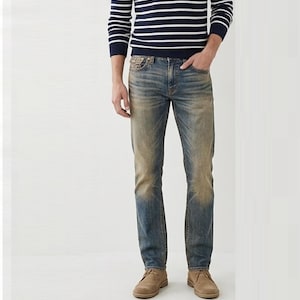 May include: A long-sleeve navy and white horizontal striped jumper paired with medium-wash blue denim jeans featuring a faded, distressed finish and tan suede shoes. The jeans have a classic five-pocket design with visible stitching.