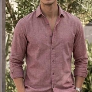 May include: A long-sleeved button-down shirt in a muted red or dusty rose color, featuring a classic collar, a front button placket, and cuffed sleeves, paired with light tan trousers and a silver-toned wristwatch on the wrist.