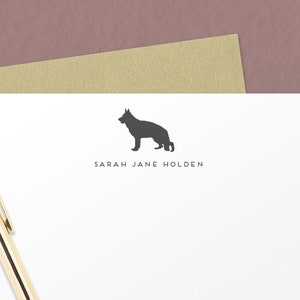 May include: A white stationery card with a black silhouette of a German Shepherd dog and the text "SARAH JANE HOLDEN" printed in black.