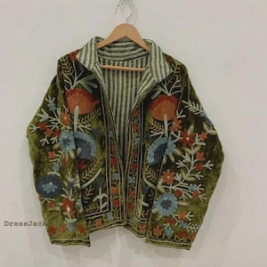 Könnte beinhalten: Eine olivgrüne Jacke mit langen Ärmeln und Kragen, verziert mit aufwendigen Blumenstickereien in Orange-, Blau- und Weißtönen. Das Innenfutter zeigt ein vertikales weiß-grünes Streifenmuster. Der Text DressJack ist deutlich zu erkennen.