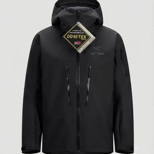 Peut inclure: Une veste à capuche noire dotée d'une fermeture éclair frontale intégrale, de deux poches poitrine verticales à fermetures éclair scellées et d'une étiquette Gore-Tex attachée au col. Le logo Arc'teryx est brodé en gris sur la poitrine.