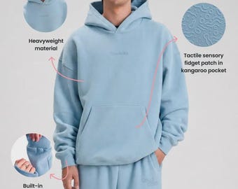 Może przedstawiać: Jasnoniebieska bluza z kapturem i pasujące spodnie dresowe. Bluza wykonana jest z ciężkiego materiału i posiada kieszeń typu kangurka z dotykową naszywką sensoryczną oraz wbudowaną piłeczkę antystresową zintegrowaną z mankietem rękawa.