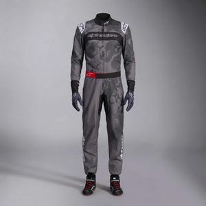 Op de afbeelding: Een grijs camouflage racepak met het Alpinestars-logo op de borst, schouders en benen. Het pak is voorzien van een zwarte kraag, een rood accent bij de taille, zwarte handschoenen en zwarte raceschoenen met rode veters en witte details.