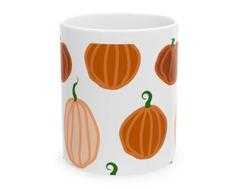 Può includere: Una tazza in ceramica bianca con un motivo ripetuto di varie zucche nei toni dell'arancione, ruggine e pesca chiaro. Ogni zucca è illustrata con linee semplici e presenta un piccolo stelo verde scuro sulla parte superiore.