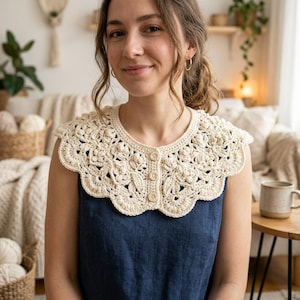May include: A cream-colored crochet collar featuring an intricate floral pattern with raised textures and scalloped edges. The collar is fastened at the front with three small, round, light brown wooden buttons and is worn over a dark blue sleeveless top.