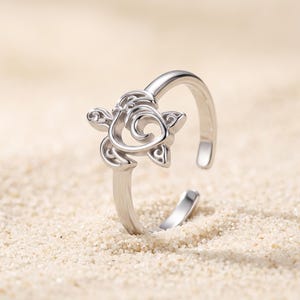 Op de afbeelding: Een zilverkleurige metalen ring met een gestileerd ontwerp van een zeeschildpad als middelpunt. De ring heeft een open band, waardoor de maat verstelbaar is. Het schildpadmotief is vervaardigd met gladde lijnen en uitgesneden details.