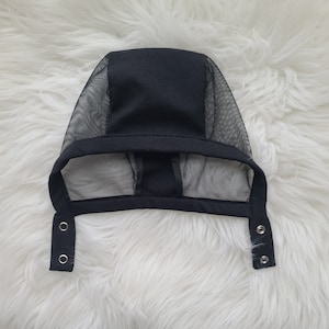 May include: Black mesh baby bonnet with a black fabric top and two snap closures on the sides.