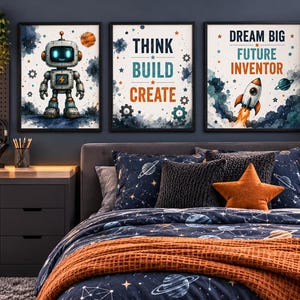 Op de afbeelding: Drie ingelijste wandposters met een robot, de tekst "THINK BUILD CREATE" en een raket met de tekst "DREAM BIG FUTURE INVENTOR". De prints hangen boven een bed met ruimtevaart-beddengoed, inclusief een donkerblauw dekbed met planeten en een oranje stervormig kussen.