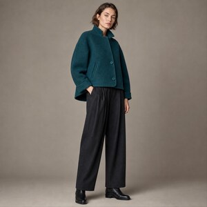 Peut inclure: Une veste courte en mélange de laine bleu sarcelle avec un col montant et deux boutons sur le devant, associée à un pantalon large gris anthracite. La veste présente des manches longues et des poches latérales, le pantalon a une taille plissée.