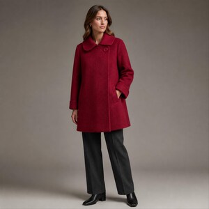 Puede incluir: Un abrigo de mezcla de lana en color rojo intenso con textura, que presenta un cuello ancho, mangas largas y un cierre de un solo botón visible en el escote. El abrigo se combina con pantalones gris carbón oscuro y botas de cuero negras.