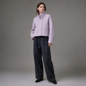 Peut inclure: Une veste courte violet clair avec un col montant et des manches longues, associée à un pantalon large gris anthracite foncé. La veste présente une fermeture frontale épurée et deux poches fendues horizontales, tandis que le pantalon est plissé.