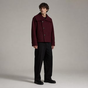 Può includere: Una giacca in misto lana color bordeaux intenso con un ampio colletto ripiegato, tre grandi bottoni scuri e maniche lunghe con polsini. La giacca è abbinata a pantaloni neri semplici e scarpe in pelle nera, creando un outfit strutturato e a strati.