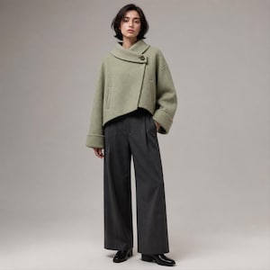 Peut inclure: Une veste courte vert sauge avec un large col rabattu, une fermeture à un bouton et des manches longues à larges poignets, associée à un pantalon gris anthracite taille haute à jambes larges avec plis et des chaussures en cuir noir.