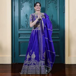 May include: A vibrant royal blue lehenga set featuring a cropped blouse with intricate silver embroidery and a matching high-waisted skirt with detailed silver floral patterns and a sheer dupatta draped over the shoulder with silver border accents.