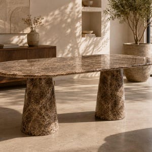 Pode incluir: Uma mesa de jantar oval com um tampo de mármore castanho polido com padrões de veios intrincados. A mesa é suportada por dois pedestais cónicos de mármore maciço a condizer, que proporcionam uma base estável para a superfície lisa.