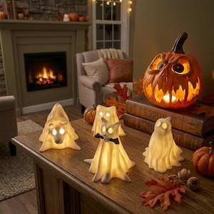 May include: A collection of four white, glowing ghost-shaped figurines and one orange carved jack-o'-lantern with a lit interior. The ghosts feature smooth, draped forms with illuminated eye cutouts, and one ghost wears a small black bow tie.