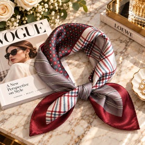 May include: A square silk scarf featuring a patchwork design with sections of deep red floral patterns, white and blue plaid, and grey diagonal stripes. The scarf is tied in a knot, displaying a smooth, lustrous finish and a solid dark red border.