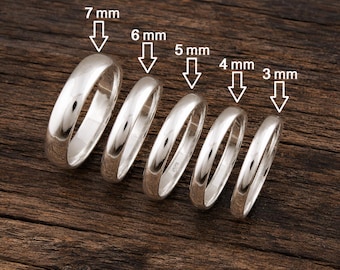 May include: Five polished silver-tone rings arranged in a row, each with a white arrow pointing to its width labelled 7 mm, 6 mm, 5 mm, 4 mm, and 3 mm. The rings have a smooth, rounded profile and a reflective metallic surface, displayed in descending order of size.