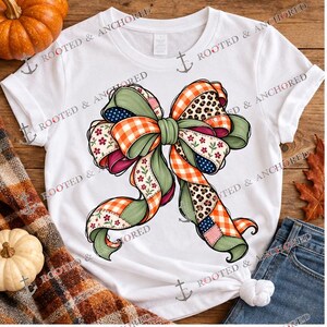 Może przedstawiać: Biały t-shirt z krótkim rękawem z dużą, centralną grafiką przedstawiającą ozdobną kokardę. Kokarda składa się z wielu wzorów tkanin, w tym pomarańczowo-białej kratki vichy, panterki, motywów kwiatowych oraz jednolitych sekcji w kolorze szałwiowej zieleni.